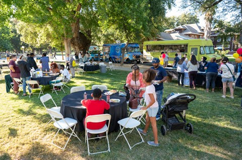 People are gathered around tables on the Olson Hall lawn for the Fall Welcome with various food trucks in the background. 