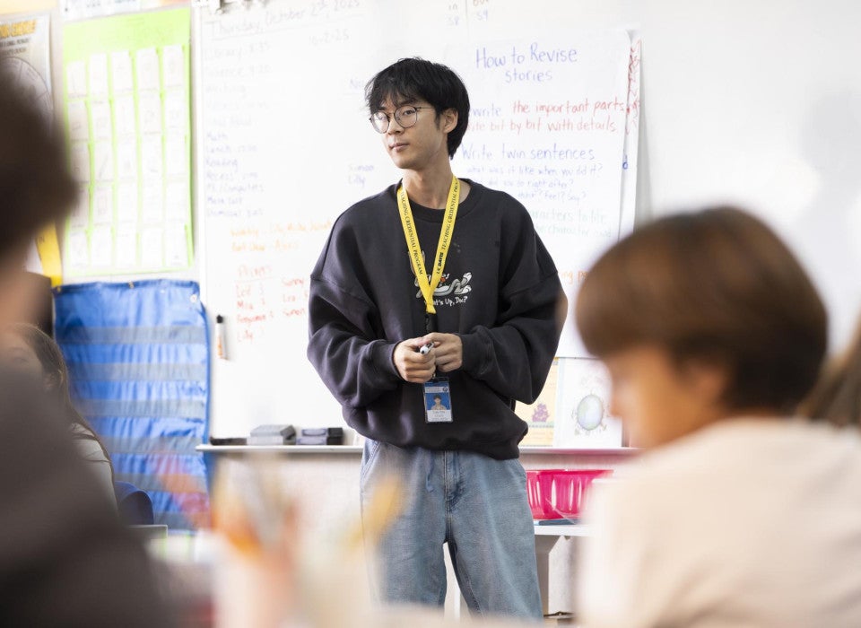 A teacher stands in front of his students who are facing the front of the classroom.